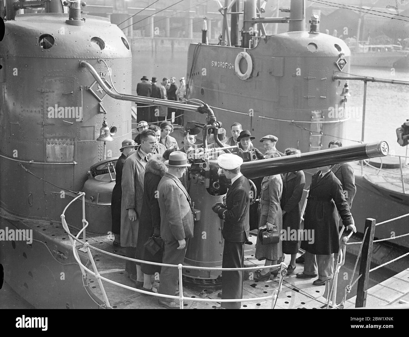 London sieht die Marine. U-Boote in Dock in der Nähe der Tower Bridge. Die U-Boote der Heimatflotte, die im Pool von London zur Krönung stationiert waren, wurden nur wenige Stunden nach ihrer Ankunft für die Besichtigung geöffnet. Fotoausstellungen: Offiziere erklären Besuchern an Bord des U-Bootes HMS Starfish (19S) im St Katharine's Dock, London, die Waffen. Ein weiteres U-Boot der Gruppe 1 der britischen S-Klasse HMS Swordfish (61S) ist im Hintergrund. Mai 1937 Stockfoto