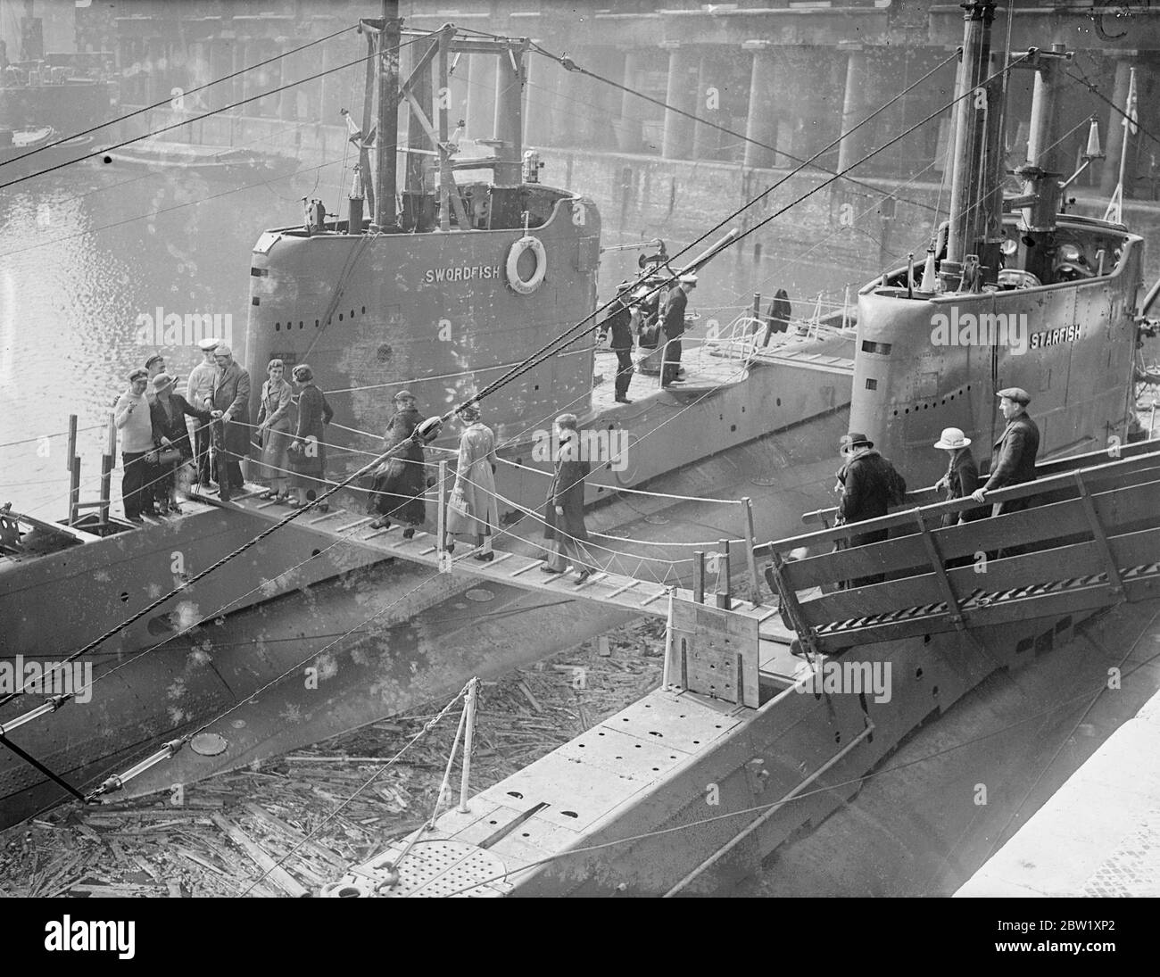 London sieht die Marine. U-Boote in Dock in der Nähe der Tower Bridge. Die U-Boote der Heimatflotte, die im Pool von London zur Krönung stationiert waren, wurden nur wenige Stunden nach ihrer Ankunft für die Besichtigung geöffnet. Fotoausstellungen: Besucher, die an Bord des U-Bootes HMS Swordfish (61S) im St Katharine's Dock, London, gehen. Ein weiteres Group One-U-Boot der britischen S-Klasse HMS Starfish (19S) schlägt sich vor. Mai 1937 Stockfoto