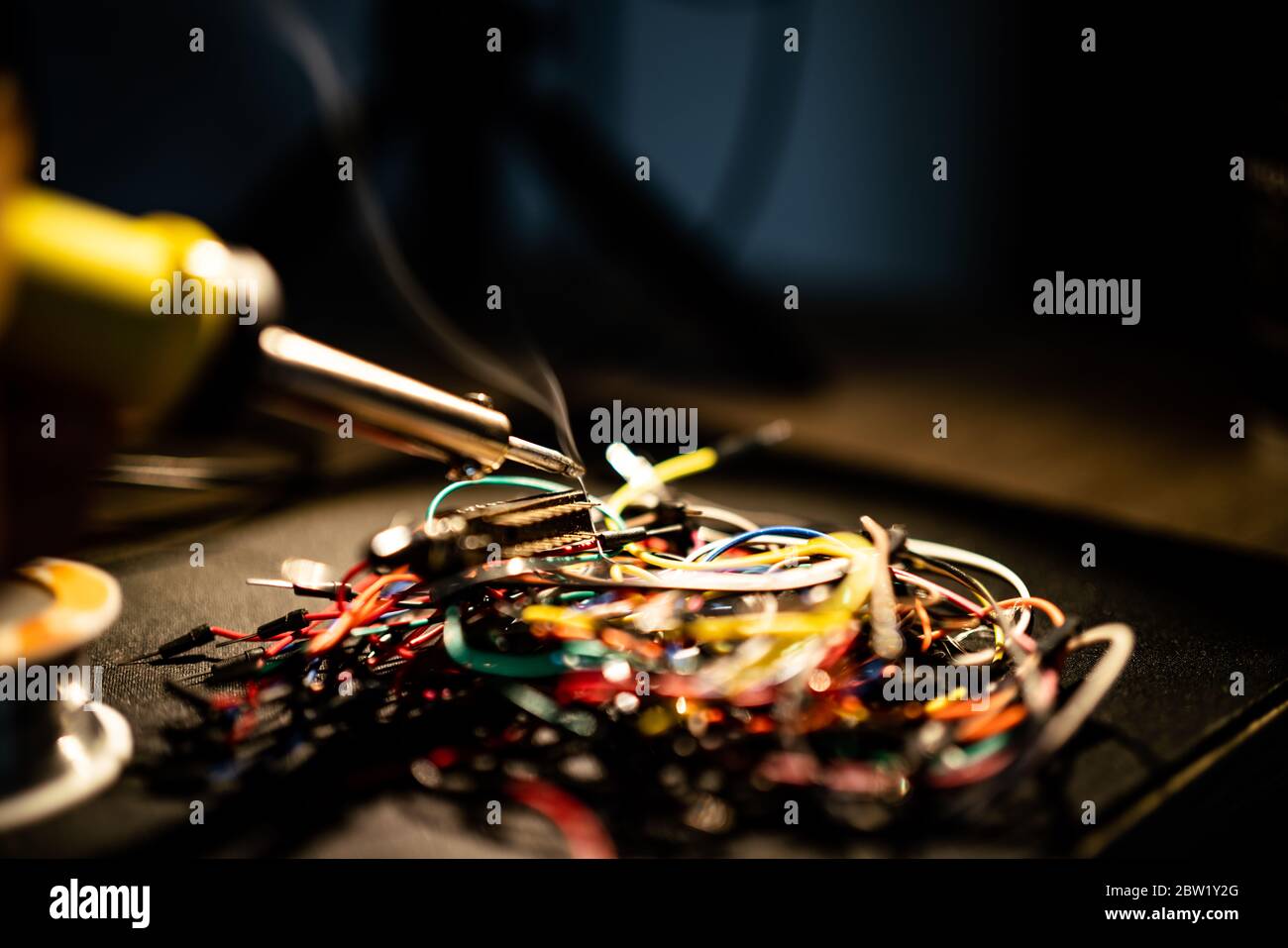 Lötkolben Löten eines Drahtes an ein elektrisches Bauteil mit Rauch, der von ihm kommt, auf farbigen Drähten liegend. Stockfoto