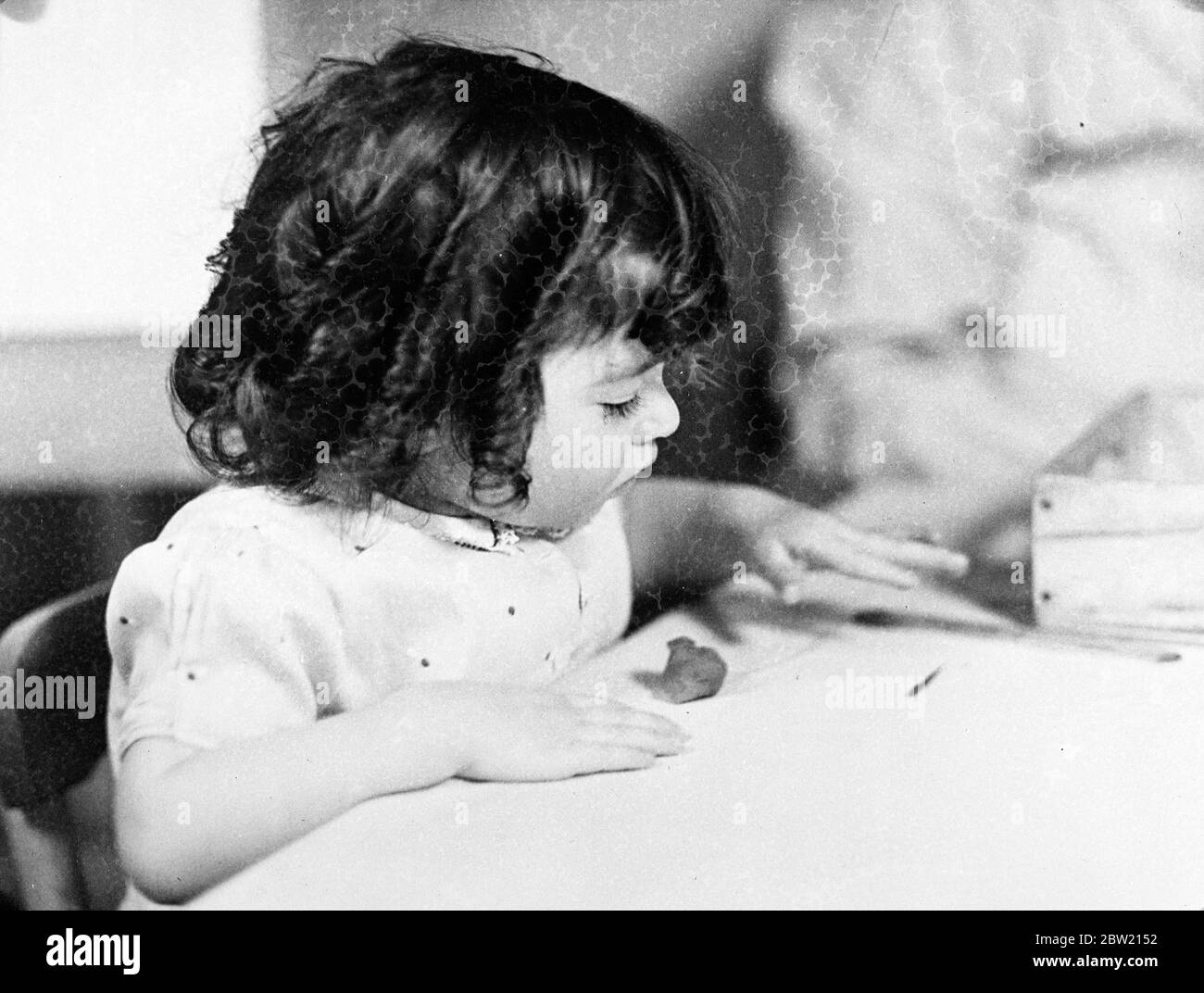 Emilie modelliert einen Klumpen Ton in der Dionne Kinderstube bei Calendar, Ontario. Die Dionee-Quintlets beginnen, den kreativen Drang zu erfahren, die mit Schmerz versorgten glücklichen Quins sind Bausteine und andere Mittel der Selbstdarstellung. 18 Juli 1937. Stockfoto