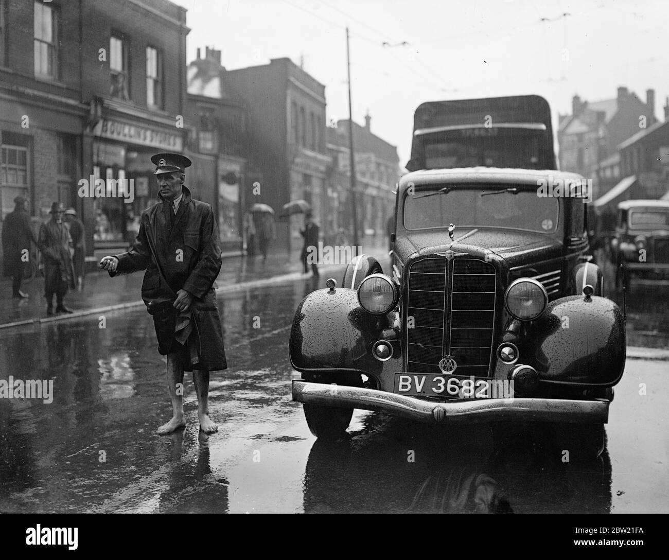 London Transport Inspektor, mit Hosen über seinen Knien versteckt, lenkt Verkehr in einer überfluteten Kingston Street nach dem schrecklichen Gewitter, das über den Heimatbezirken platzte und die Stadt überflutete. 13 Juli 1937 Stockfoto