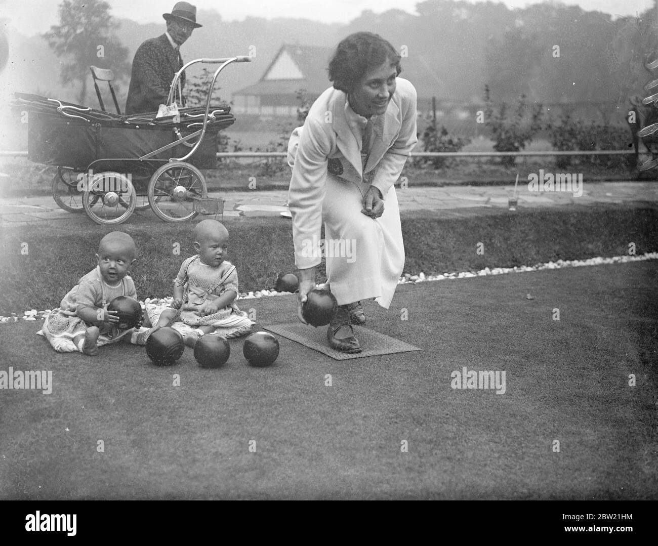 Jacqueline (links) bereitet sich darauf vor, Frau Hallet eine weitere Schüssel zu übergeben, während Jill ihre Mutter im Spiel beobachtet. Die zehn Monate alten Zwillinge begleiteten ihre Mutter, als sie bei den Einzelveranstaltungen der National Bowls Championships der Frauen im Wimbledon Park, London, antrat. Bis 26. August 1937 Stockfoto