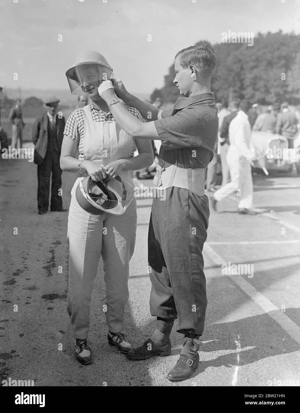 Herr A.C Dobson justiert den Helm seiner Frau, bevor sie mit ihrem Fiat die Strecke nahm. Das erste Mal in seiner Geschichte fand in England der Royal Automobilclub International Tourist Trophy Race auf der Donington Park Road Circuit in der Nähe von Derby statt. Die einzige Frau, die den 310 Meilen langen Kurs bedeckte, war Mrs A.C Dobson. September 1937. Stockfoto