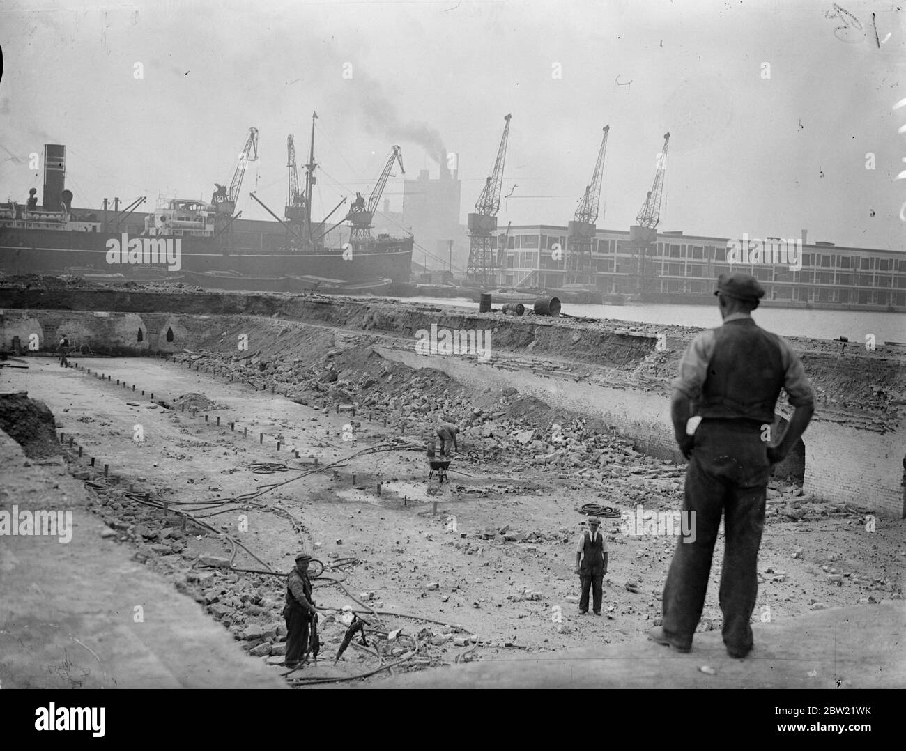 Ein allgemeiner Blick, wie Arbeiter die alten Steinstege, deren Fundamente weggesprengt werden sollen, in den Royal Victoria Docks demolierten. Kosten Â£1,500,000 die modernste Dock in der Welt wird unter dem Port of London Behörde Verbesserung Schema gebaut. Während der zwei Jahre wurden die Arbeiten an dem System, in dem 600 Männer an Eisenbahntunneln unter dem Dock gearbeitet haben, ohne den Verkehr zu stören, gesenkt. September 1937 Stockfoto