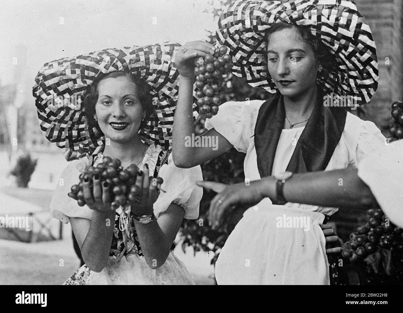 Zwei hübsche italienische Mädchen in Bauerntracht und breiten Hüten mit Krempe bieten während des Weinfestes Trauben für Passanten in Rom zum Verkauf an. 21. September 1937. Stockfoto
