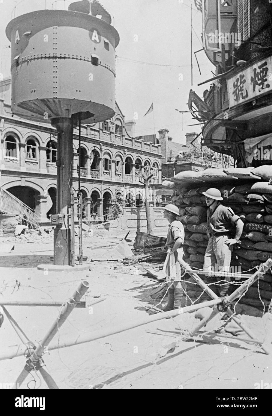 Britische Soldaten hätten in Shanghai durch japanische Bombe beinahe ausgelöscht. Britische Soldaten, die einen Posten an der Ecke Kiangse Road und Range Road besetzen, gratulierten sich zu einer der engsten Fluchten, die ausländische Truppen während der Kämpfe in Shanghai erlebt haben. Eine Luftbombe, die von einem japanischen Kriegsflugzeug für einen chinesischen Scharfschützenposten in der Nähe vorgesehen war, verpasste ihr Ziel und explodierte mitten auf der Straße. Das Brighton ist eine wunderbare Flucht vor der Ausrottet. Foto zeigt, die britische Post an der Ecke der Kiangse Road und Range Road, Shanghai. Soldaten vermessen die Schäden, die durch die Japane verursacht wurden Stockfoto
