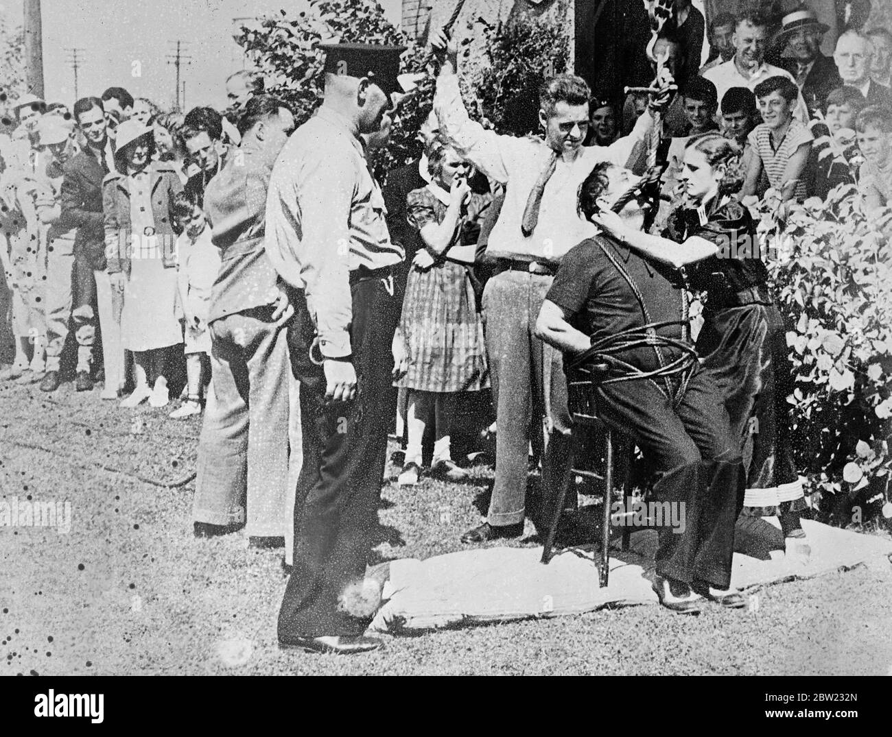 Ein Mädchen und Schlinge um den Hals der gebundenen Ovette befreite er dann seinen Hals von der Schlinge, nachdem er die Bindungen losgelassen hatte, die ihn an den Stuhl fesselten. Joseph Ovette aus ottawa ließ sich von einer Menge in Fort Erie, Kanada, lynchen, aber nur um eine seiner neuesten Stunts zu demonstrieren, denn er ist ein professioneller Zauberer. 17. September 1937.[?] Stockfoto