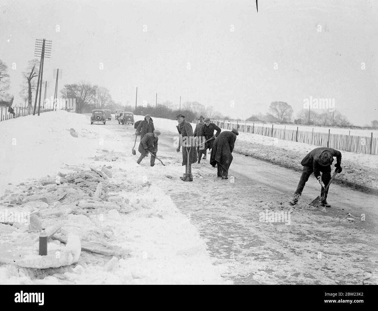 Ein 20-stündiger Schneesturm hat in Kent zu einer schweren Verrenkung geführt, wo Dörfer fast abgeschnitten wurden und Straßen durch Schneeverwehungen blockiert wurden, die in einigen Bezirken bis zu 8 Fuß tief sind. Viele Häuser sind komplett isoliert. Schneepflüge und Männerbanden mussten gestrandete Autofahrer zur Rettung bringen. Foto zeigt, Schnee von der Hauptstrasse Londons, Folkestone Road in Lenham zu räumen. 16 Februar 1938 Stockfoto