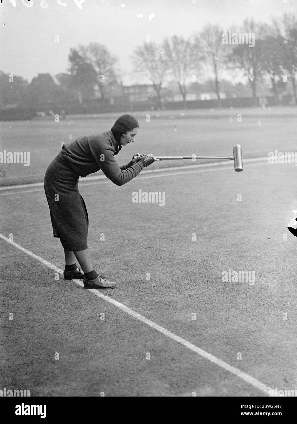 Für das Wetter gekleidet, bei Roehampton Croquet. Frauen, die sich für das Wetter gekleidet haben, das eher kühl war, als sie am Peel Memorial Croquet Meeting im Roehampton Club, London, teilnahmen. Foto zeigt Frau M Longman, die einen Hut im Balaclava-Stil trägt, wenn sie den Schuss macht. Mai 1938 Stockfoto