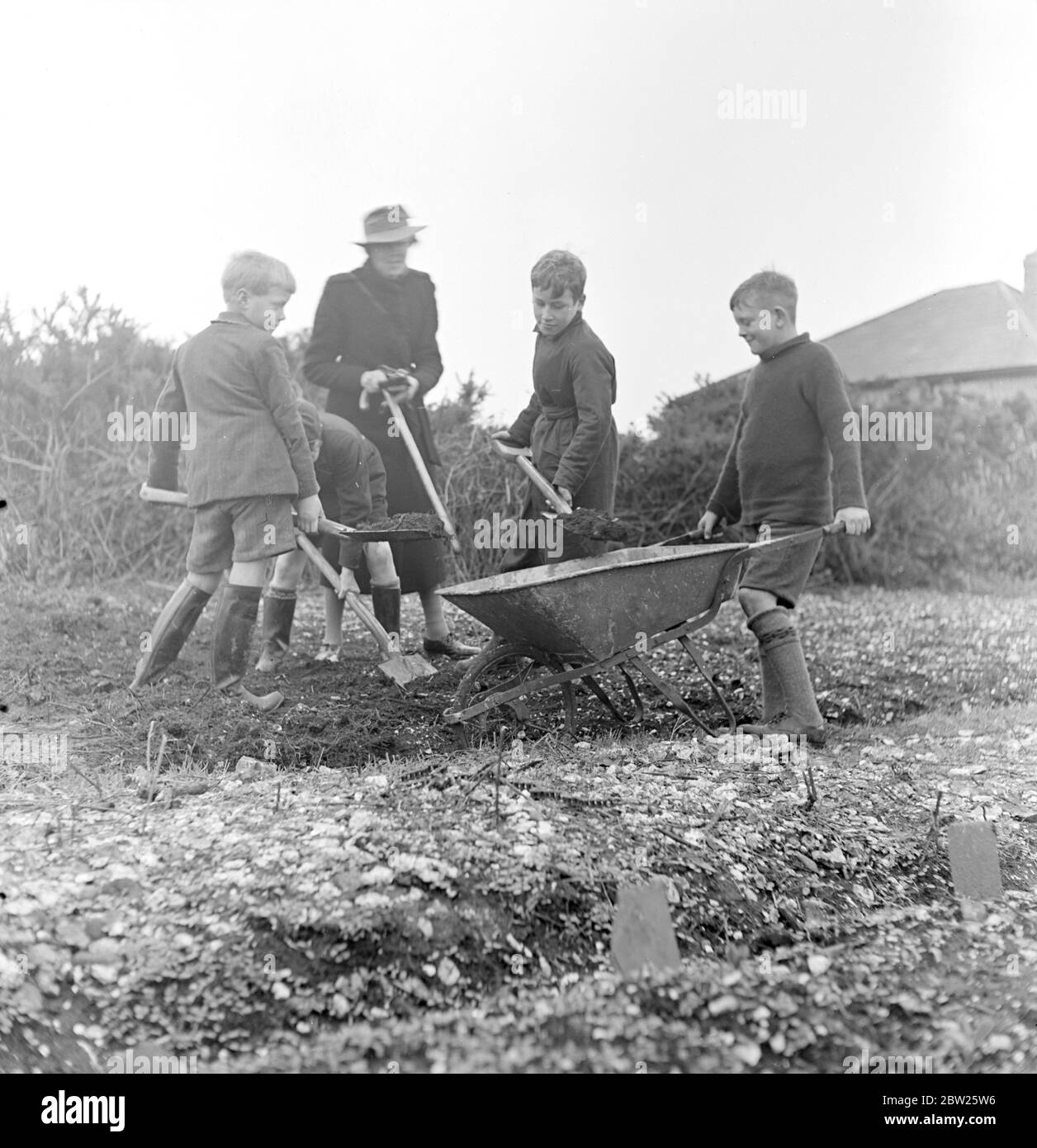 Cockney-Kinder aus der Sydenham Road-Gegend von Croydon werden nach der Evakuierung in die Woodingdean-Gegend bei Brighton zu Bauern. Miss Leago übersieht die Jungs, die Erde in den Lauf schaufeln. Stockfoto