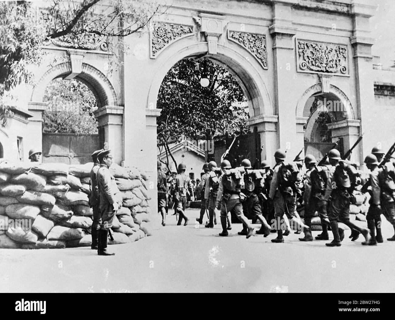 Im Kampf zwischen Chinesen vor den Toren Pekins fliehen Hunderte von Flüchtlingen, während japanische Truppen Waffen und Ausrüstung tragen, die aus der japanischen Gesandtschaft herausmarschieren. 13 Juli 1937. Stockfoto