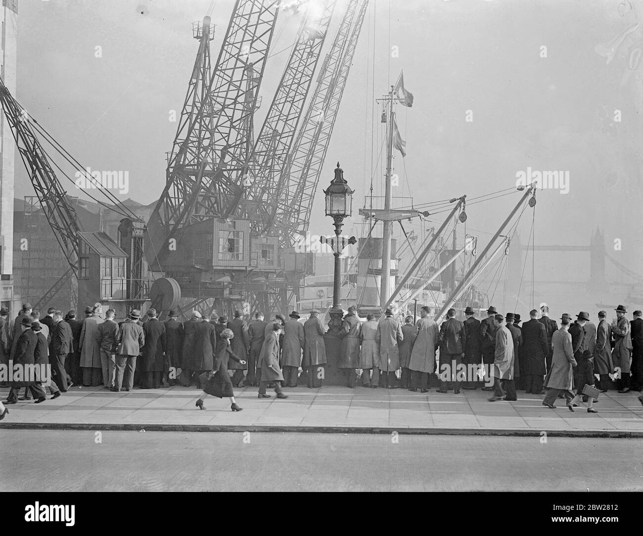 Mittagspause in der Sonne im Januar. Eine Menge Stadtarbeiter säumen die London Bridge, um ihre Mittagsstunde im Unerwarteten zu verbringen. Januar Sonnenschein beobachten das Entladen der Schiffe im Pool. Im Hintergrund ist Tower Bridge. 17. Januar 1938 Stockfoto