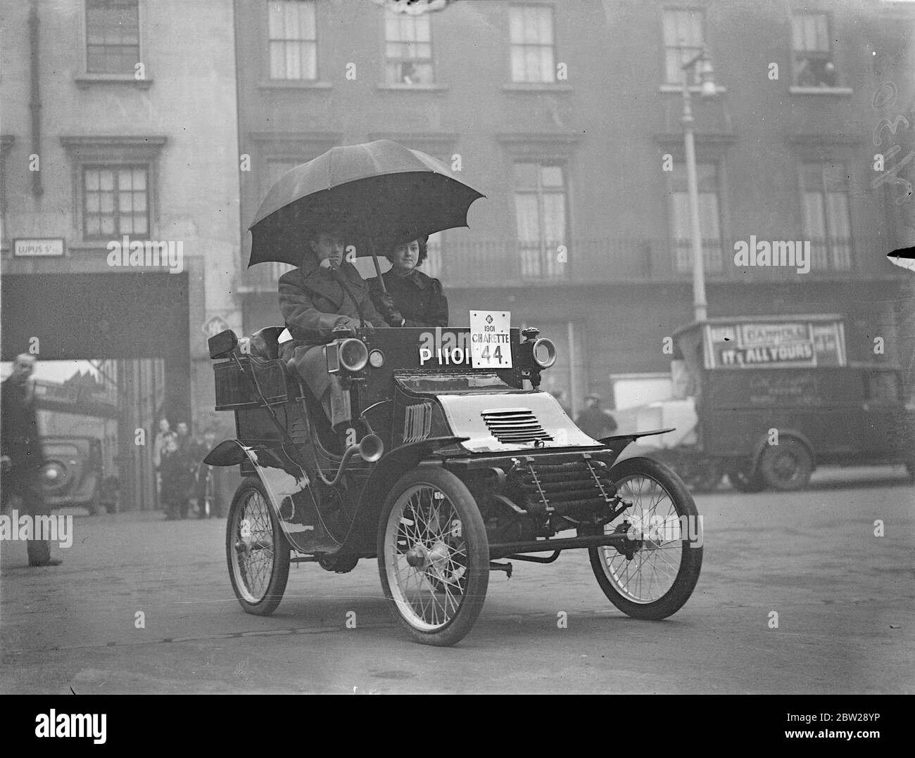 „Old Crocks“ wurde vor dem London Brighton Run genau unter die Lupe genommen. "Alte Schrocken", die morgen (Sonntag) an der jährlichen Gedenkveranstaltung der Royal Automobile Clubs von London nach Brighton teilnehmen sollen, kamen in der RAC-Ingenieurabteilung in der Lupas Street, Plimlico, an, um von den Abnahme-Experten untersucht zu werden. Ein Rekord von 116 Fahrzeugen, die jeweils mindestens 33 Jahre alt sind, wurde von der Organisation des Laufs empfangen, der an den 41. Jahrestag der ursprünglichen Emanzipation im Jahr 1896 erinnert. Foto zeigt, dass eine Beifahrerin auf einer Charette aus dem Jahr 1902 einen übergroßen Regenschirm als Unterschlupf benutzt, als sie entdeckt, dass es kein Wort auf der Th gibt Stockfoto