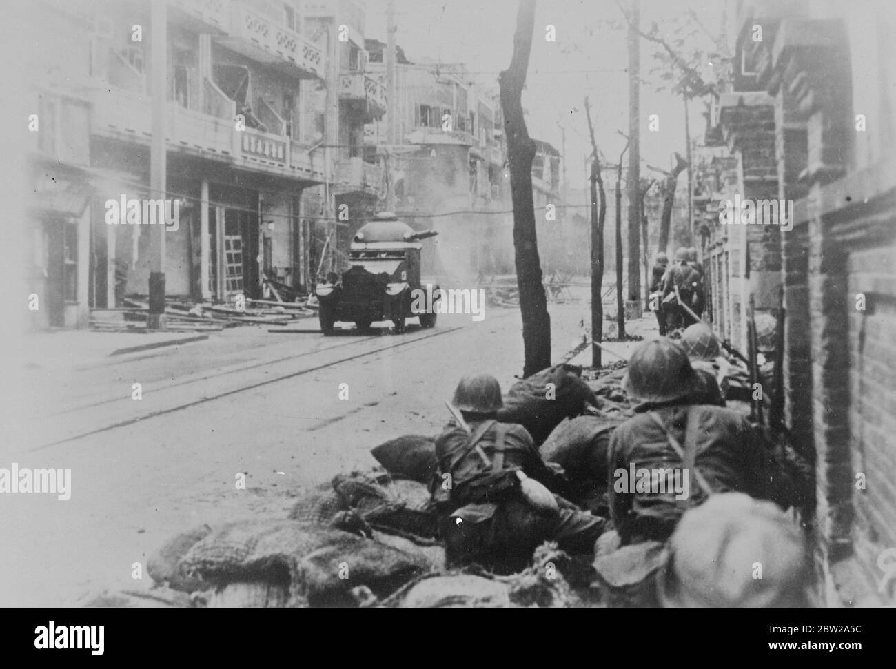 Japanische Matrosen und gepanzerte Auto 'mop up' Chinesisch. Japanische Matrosen hocken auf dem Bürgersteig einer zerstörten Shanghai Street, als sie mit Hilfe eines gepanzerten Autos den letzten der chinesischen Verteidiger, die in der Stadt verblieben sind, 'aufdecken'. 22. November 1937 Stockfoto