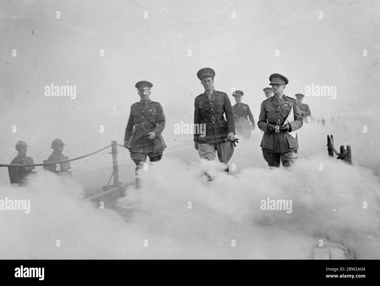 König Leopold geht durch einen Nebelwand. König Leopold von den Belgiern, nimmt an den großen Manövern der belgischen Armee im Bezirk Namur Teil. Foto zeigt, König Leopold (Mitte), der durch einen Nebelwand geht, während er eine Pontonbrücke über die Maas bei Jambes lez Namur überquert. Links ist General Denis, der Kriegsminister. 28. Oktober 1937 Stockfoto
