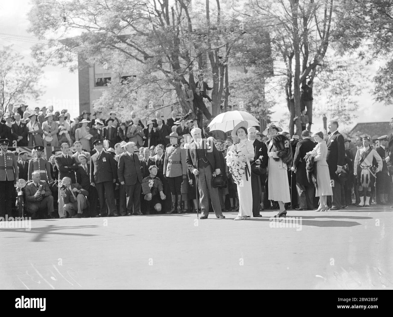 Zum ersten Mal auf der Kanada-Tour fand die Queen die Sonne heiß genug, um einen Sonnenschirm in Victoria, British Columbia, zu benötigen. Hier überreichte der König der Royal Canadian Navy im Beacon Hill Park, Victoria, die Farbe des Königs. Dahinter steht der kanadische Premierminister Mackenzie King. Juni 1939 Stockfoto