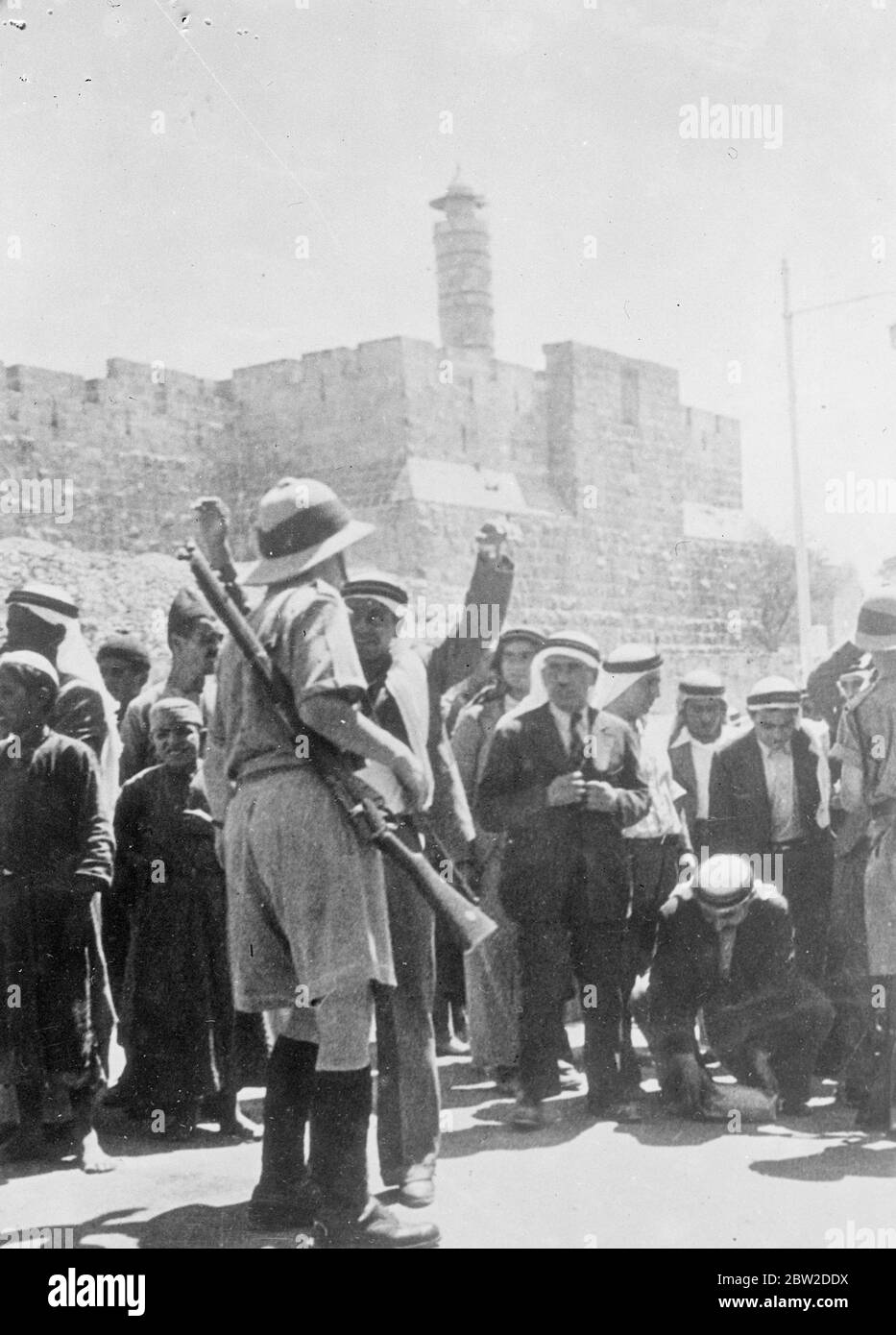 Viele Verhaftungen wurden vorgenommen, als Araber eine Demonstration in Jerusalem veranstalteten. Britische Soldaten durchsuchten jeden Demonstranten gründlich nach Waffen oder Beweisen terroristischer Aktivitäten. Foto zeigt: Ein Araber, der die Arme hochhält, als er von einem britischen Soldaten in Jerusalem durchsucht wurde. Andere Demonstranten schauen auf den 15. Oktober 1938 Stockfoto