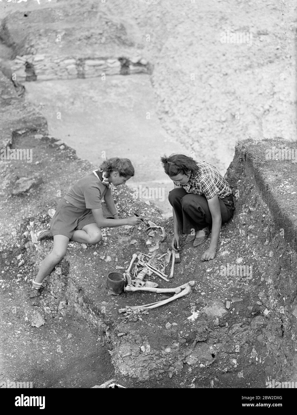 Zwei Schülerinnen hetzen ein neu gefundenes 2000 Jahre altes Skelett am östlichen Tor der Jungfernburg auf, wo neue Entdeckungen gemacht werden. Die Überreste von 2000 Jahren alten Grabstätten, in denen Skelette von Töpferwaren begleitet werden, sind schnell auf der Erde, sie wurden am östlichen Tor der Jungfernburg in der Nähe von Dorchester (Dorset) gefunden. Diese Feststellung ist ungefähr auf die römische Eroberung datieren. Bis 14. August 1937. Stockfoto
