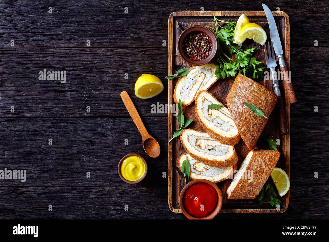Gebackene Omelette Roll mit Hühnerfleisch auf einem unfreundlichen rustikalen Holztablett serviert mit Zitrone, Tomatensauce und Senf auf einem Holztisch, horizontale Ansicht Stockfoto