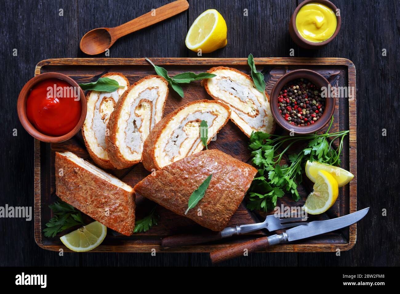 Gebackene Omelette Roll mit Hühnerfleisch auf einem unfreundlichen rustikalen Holztablett serviert mit Zitrone, Tomatensauce und Senf auf einem dunklen Holztisch, horizontal Stockfoto