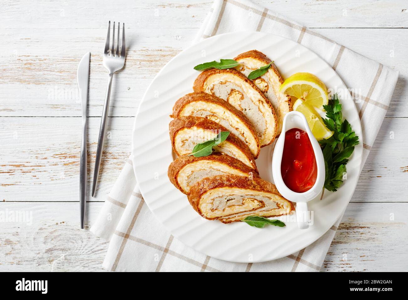 Omelette Käse Rolle mit Hackfleisch Füllung auf einem weißen Teller mit Zitrone, Tomatensauce und Petersilie auf rustikalem Holztisch, Blick auf die Landschaft, flache Lage, Stockfoto