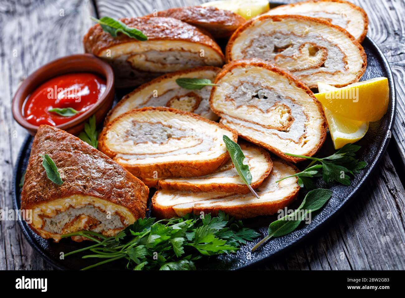 Omelette Käse Rolle mit Hackfleisch Füllung auf einem schwarzen Teller mit Zitrone, Ketchup und Petersilie auf grauen Holztisch, Blick auf die Landschaft, Nahaufnahme Stockfoto