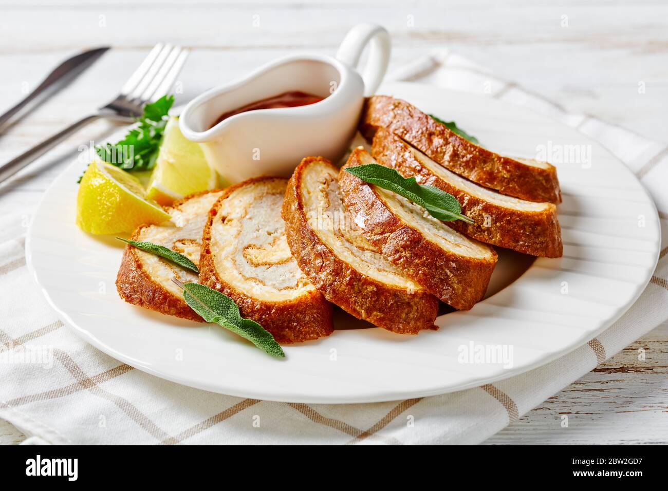 Nahaufnahme von Omelette Käse Roll mit Hackfleisch Füllung auf einem weißen Teller mit Zitrone, Tomatensauce und Petersilie auf rustikalem Holztisch, Blick auf die Landschaft Stockfoto