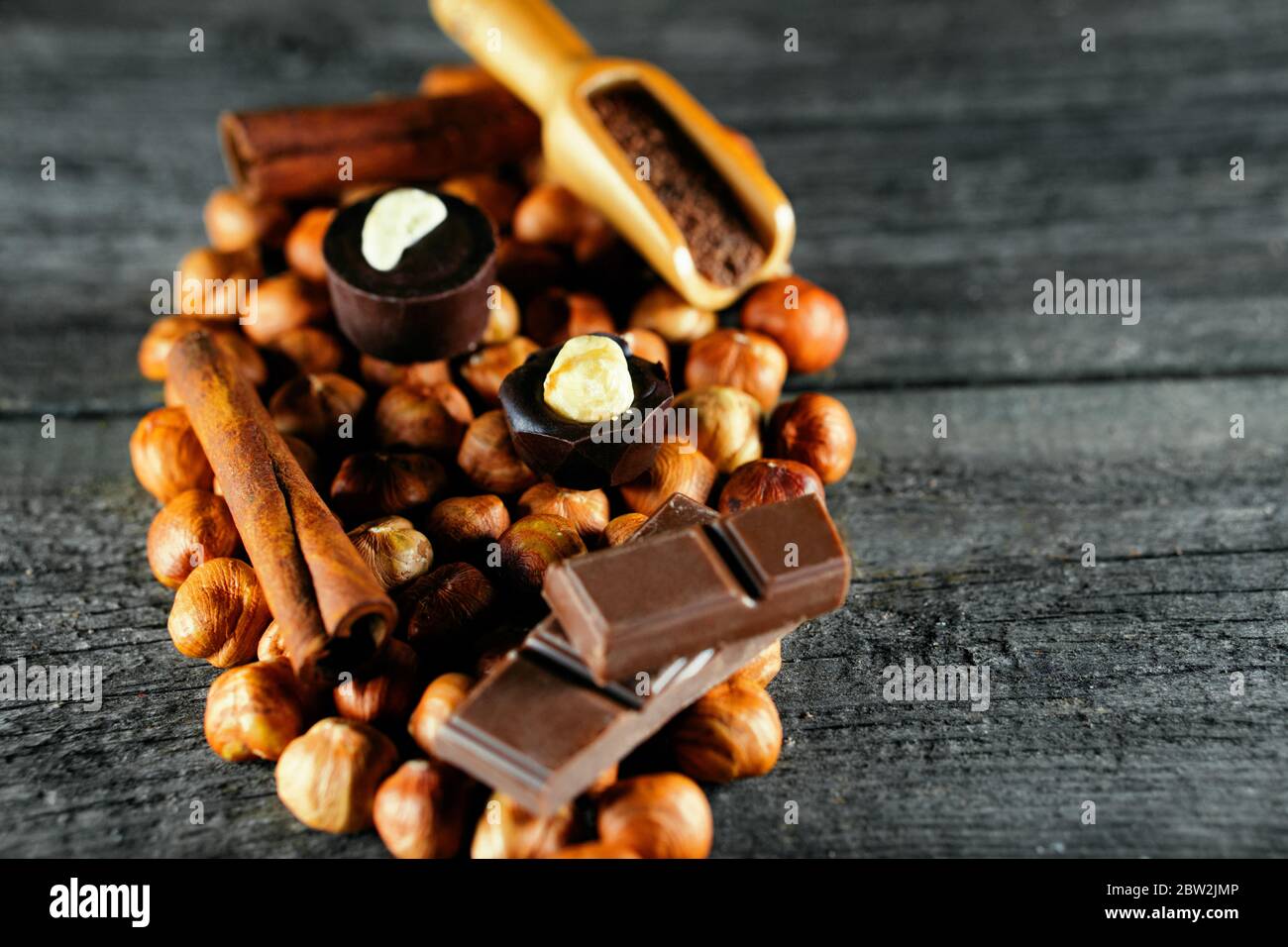 Handgefertigte Schokolade Süßigkeiten mit Haselnuss auf der Oberseite, stehen auf Haselnüssen. Schokolade Bonbons mit Schokolade, Zimt daneben auf Vintage Holz Hintergrund Stockfoto