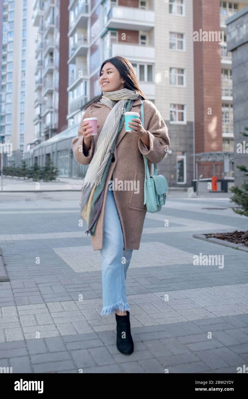 Brunette Frau in beige Mantel hält Kaffeetasse, genießen ihren Drink, Spaziergang entlang der Straße Stockfoto