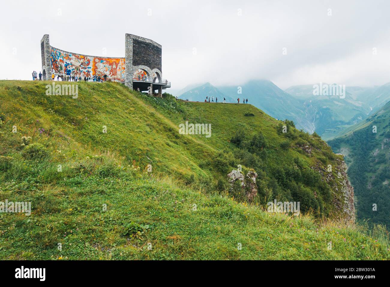 Touristen besuchen das Russland-Georgien-Freundschaftsdenkmal im Kaukasus-Gebirge, Georgien, an einem bewölkten Tag Stockfoto