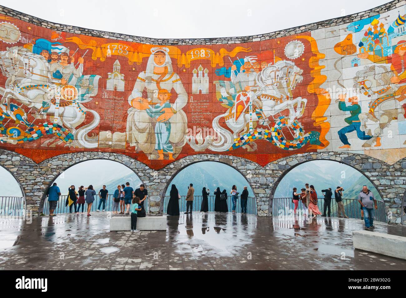 Touristen stehen unter den Bögen des Russland-Georgien-Freundschaftsdenkmals im Kaukasus, Georgien. Erbaut 1983 Stockfoto