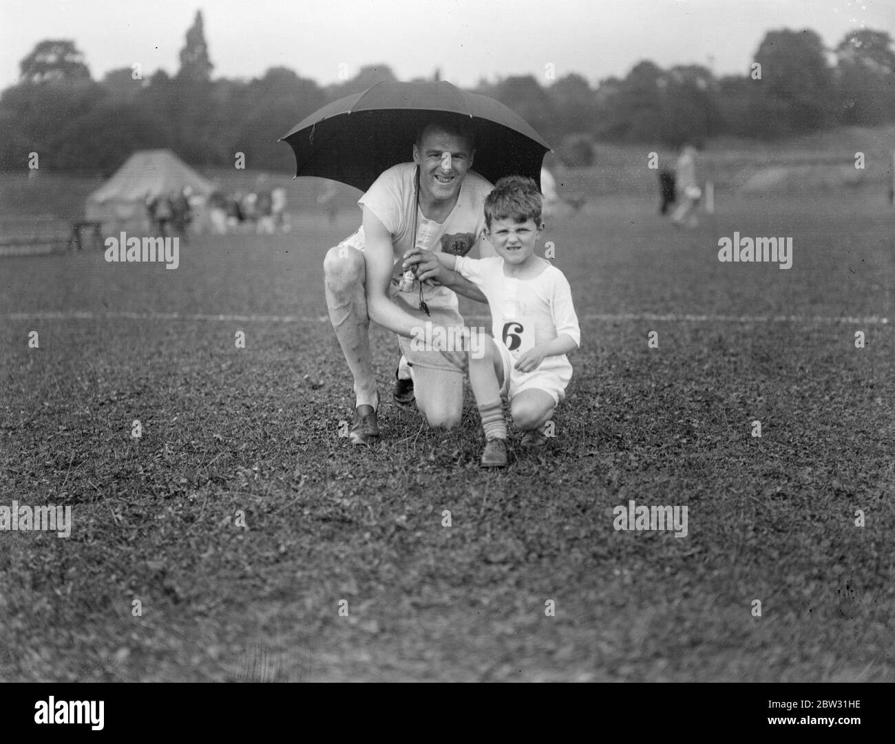 Champion und sein Sohn schützen vor dem Regen. Herr H S Preis ehemaliger Champion der South London Harriers, und sein kleiner Sohn John, im Alter von 5 1/2 , beide waren Konkurrenten in der Z-Division Metropolitan Police Sport in Crystal Palace, London , Schutz vor dem Regen unter einem Regenschirm . 27 Juli 1932 Stockfoto