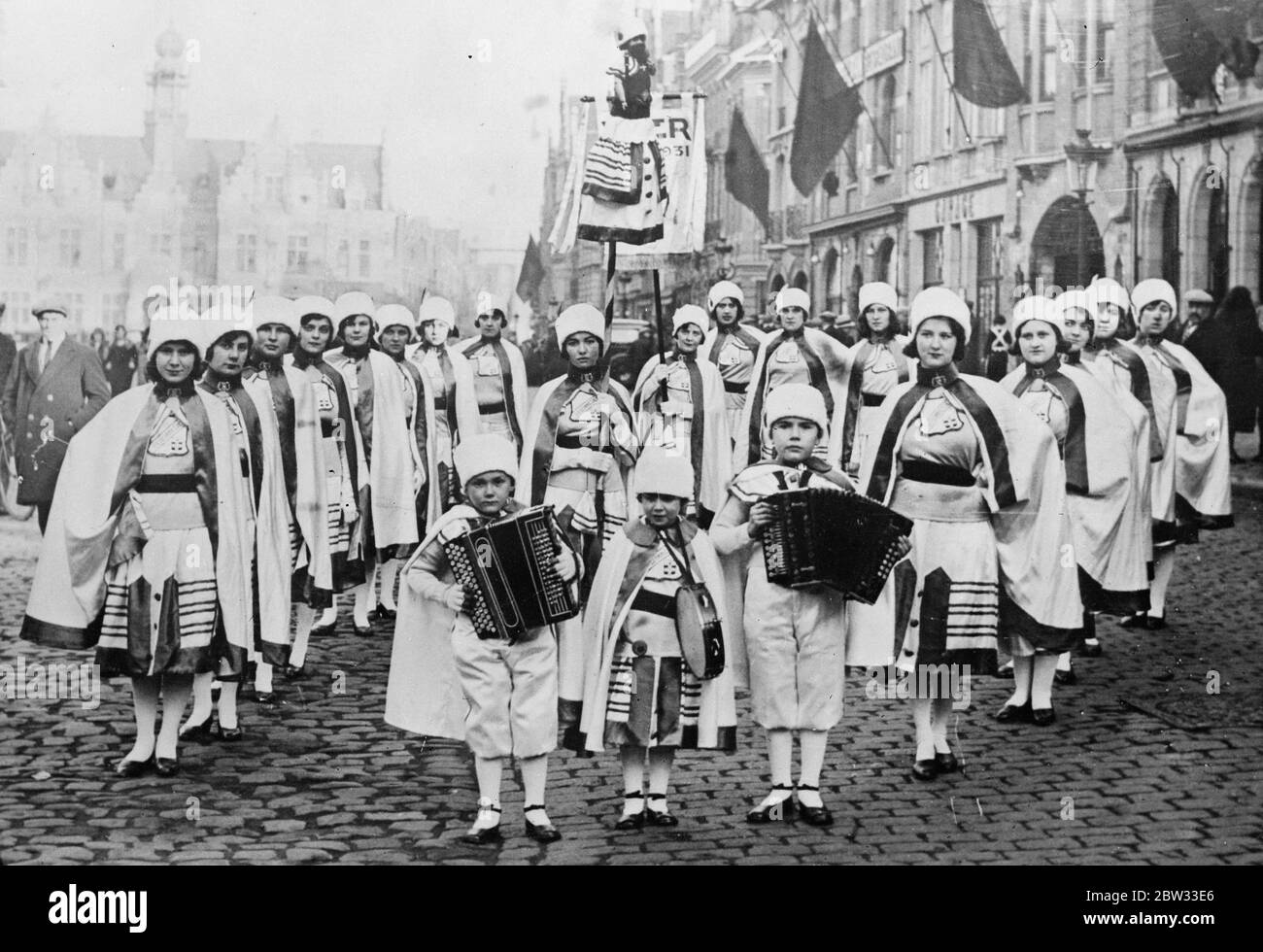 Kleine Musiker am Ypern Karneval. Drei kleine Musiker, gefolgt von Mädchen in Nationalkleidung an der Spitze der großen jährlichen Ypern-Prozession und Karneval in Belgien. Februar 1932 Stockfoto