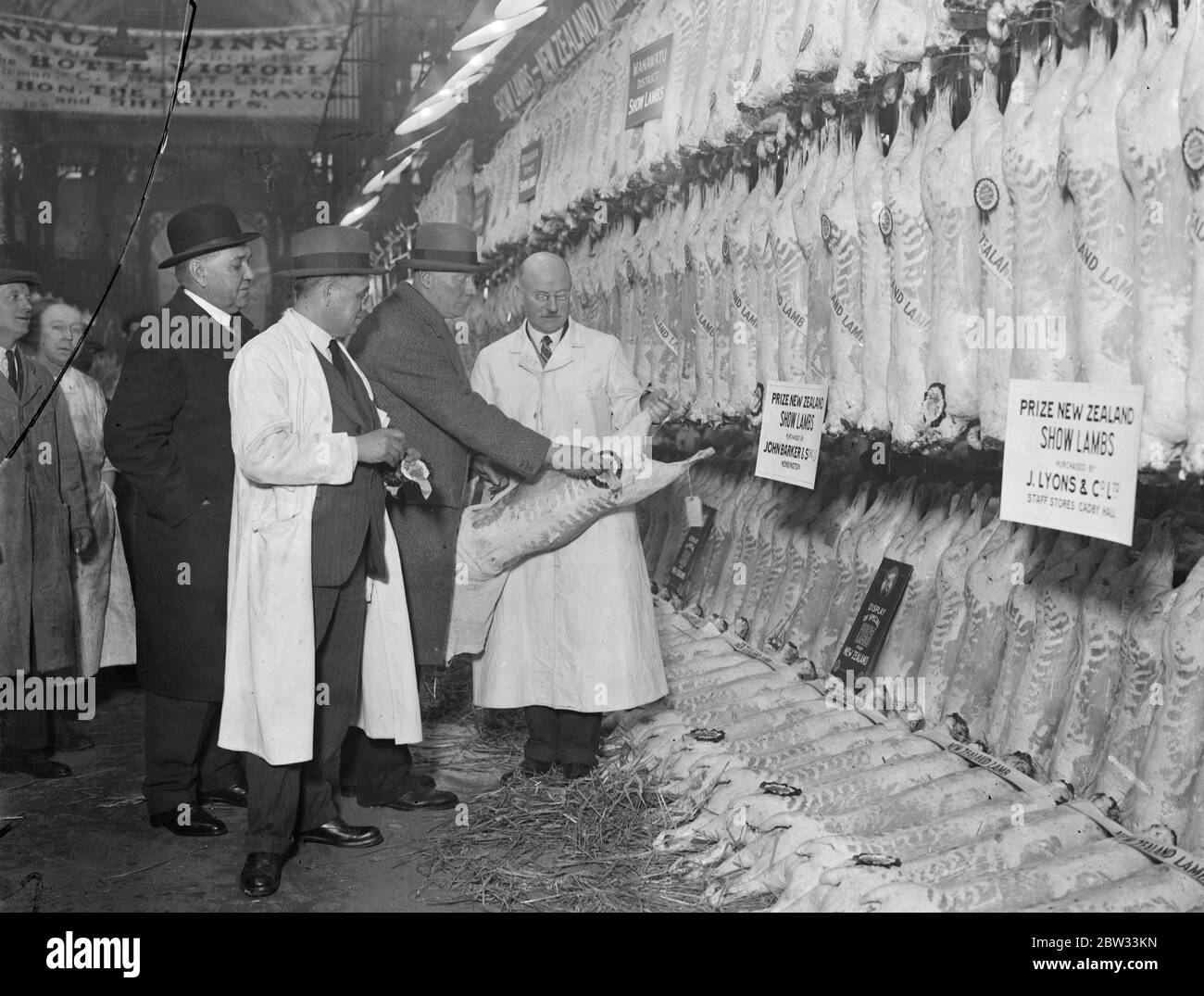 High-Speed-Wettbewerb bei Smithfield Fleisch Markt. Neunhundert Lamm Schlachtkörper wurden hng , und von drei Richtern im Namen des New Zealand District inspiziert , Schild Wettbewerb, um die besten Exponate zu wählen, um eine Herausforderung Schild und Preise erhalten , Auf dem Smithfield Market wurde der Wettbewerb vom New Zealand Meat Producers Board gefördert, um die Aufrechterhaltung eines hohen Zuchtstandards für den britischen Markt zu fördern. Die Ergebnisse wurden sofort nach Neuseeland zu den Landwirten drahtlos. Lämmer werden von den Sachverständigen, Herrn George Goodchild, Herrn W T Johnson und Herrn D C Meddent, beurteilt Stockfoto