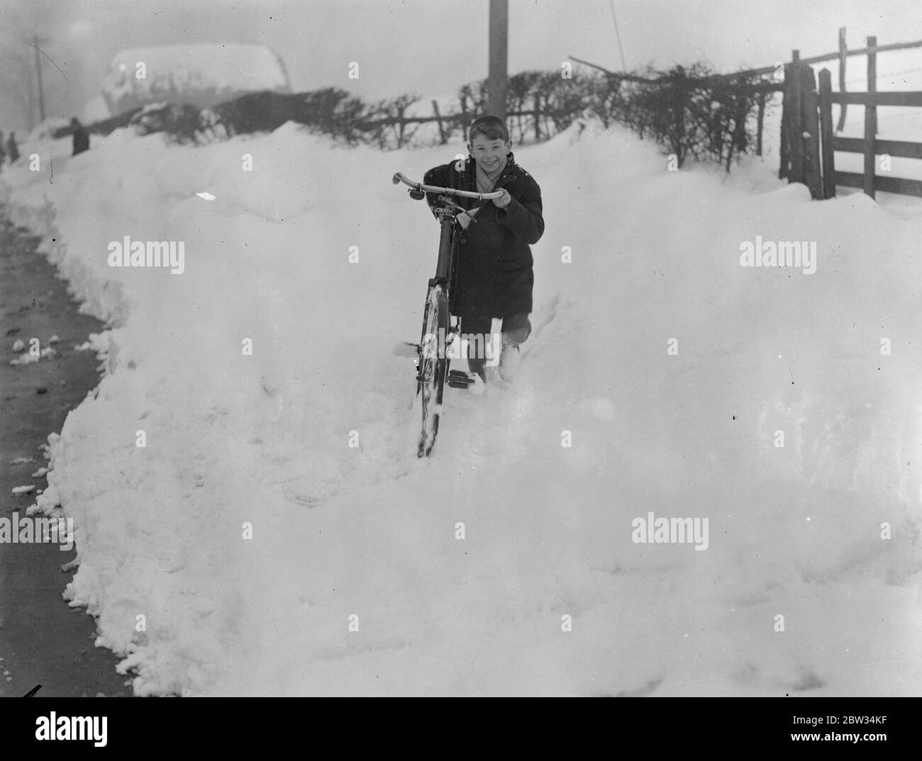 Drifts von Schnee vier Meter tief Block Surrey Straßen zum Verkehr. Drifts von Schnee mehr als vier Fuß in der Tiefe haben Straßen in Surrey und Kent blockiert und machte sie unpassierbar für den Verkehr, Armeen von Männern sind bei der Arbeit Clearing der Straßen. Ein kleiner Junge kämpft auf seinem Fahrrad durch den Schnee. 13 Februar 1932 Stockfoto