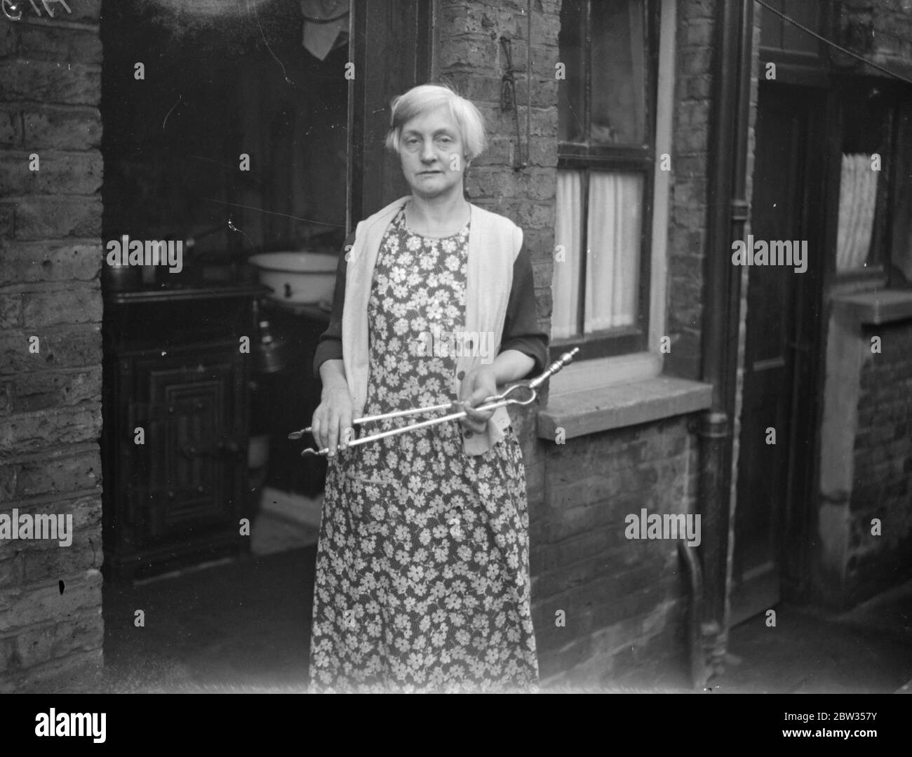 Frau schlug bewaffnete Banditen mit Feuerzangen. Eine Frau bewaffnet witth Feuertänger angegriffen einen bewaffneten Banditen, während er ihren Mann in seinem Haus in Sugden Road, Lavender Hill, London beraubt, und schlug ihn. Sie war Frau A Bateman. Der Schütze zwang sich mit einem Revolver in das Haus und verlangte Geld. Während Herr Bteman einige bekam, beobachtete Frau Bateman einige schwere Zangen und verletzte den Schützen so schwer, dass er floh. Mrs A Bateman mit der Zange, mit der sie den Schützen auf ihrem Lavender Hill nach Hause geführt hat. 27 Februar 1933 Stockfoto