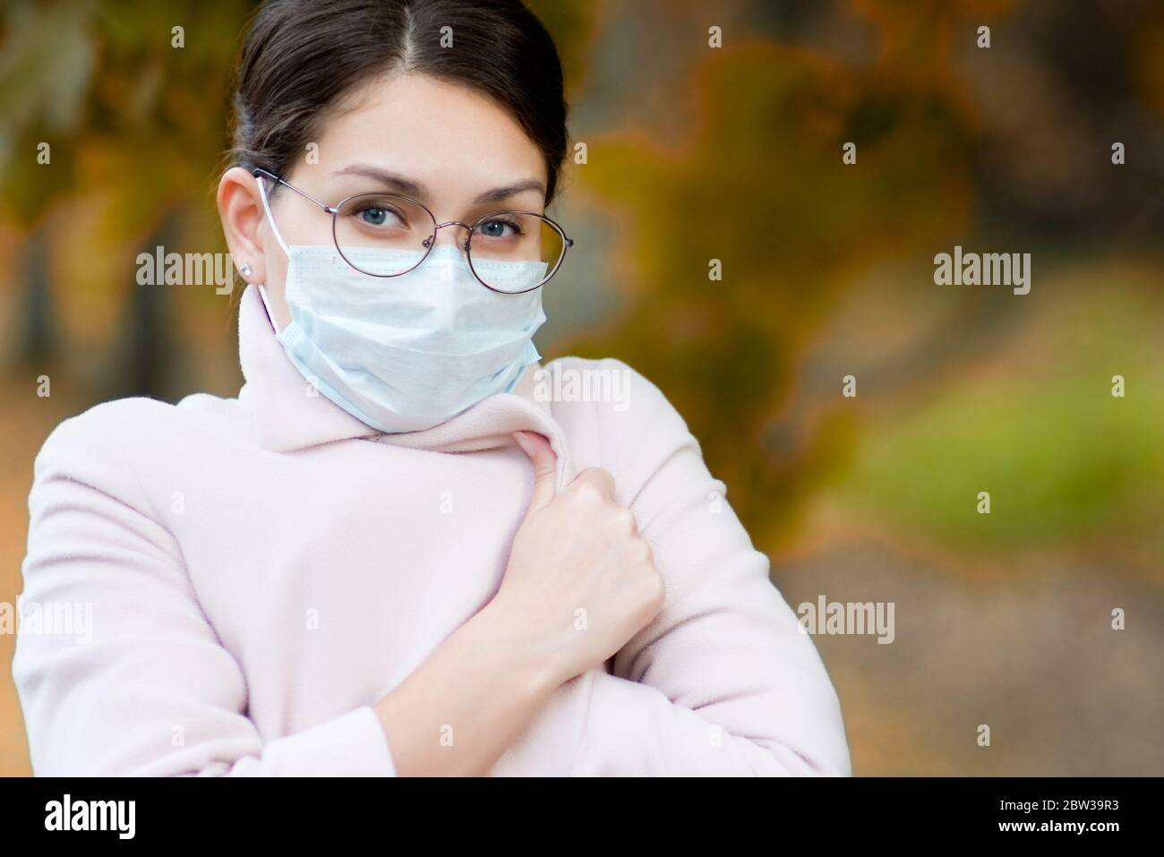 Porträt eines jungen Mädchens in einer medizinischen Maske und Brille auf einem Hintergrund der Herbstlandschaft, Nahaufnahme Stockfoto