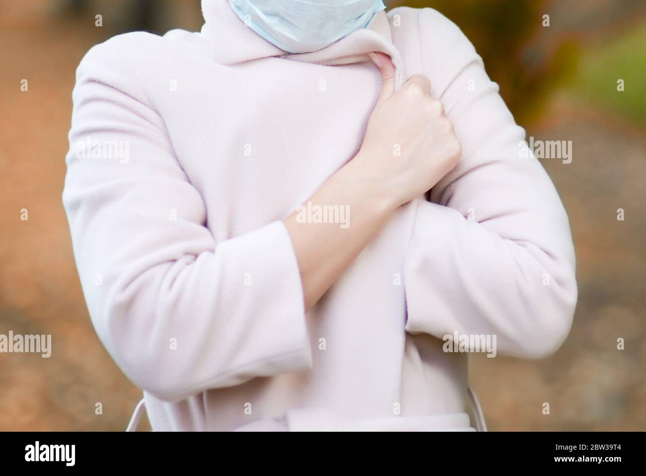 Nahaufnahme der Hände einer Frau, die ihren Mantelkragen gegen eine verschwommene Herbstlandschaft dicht verschlossen hat Stockfoto