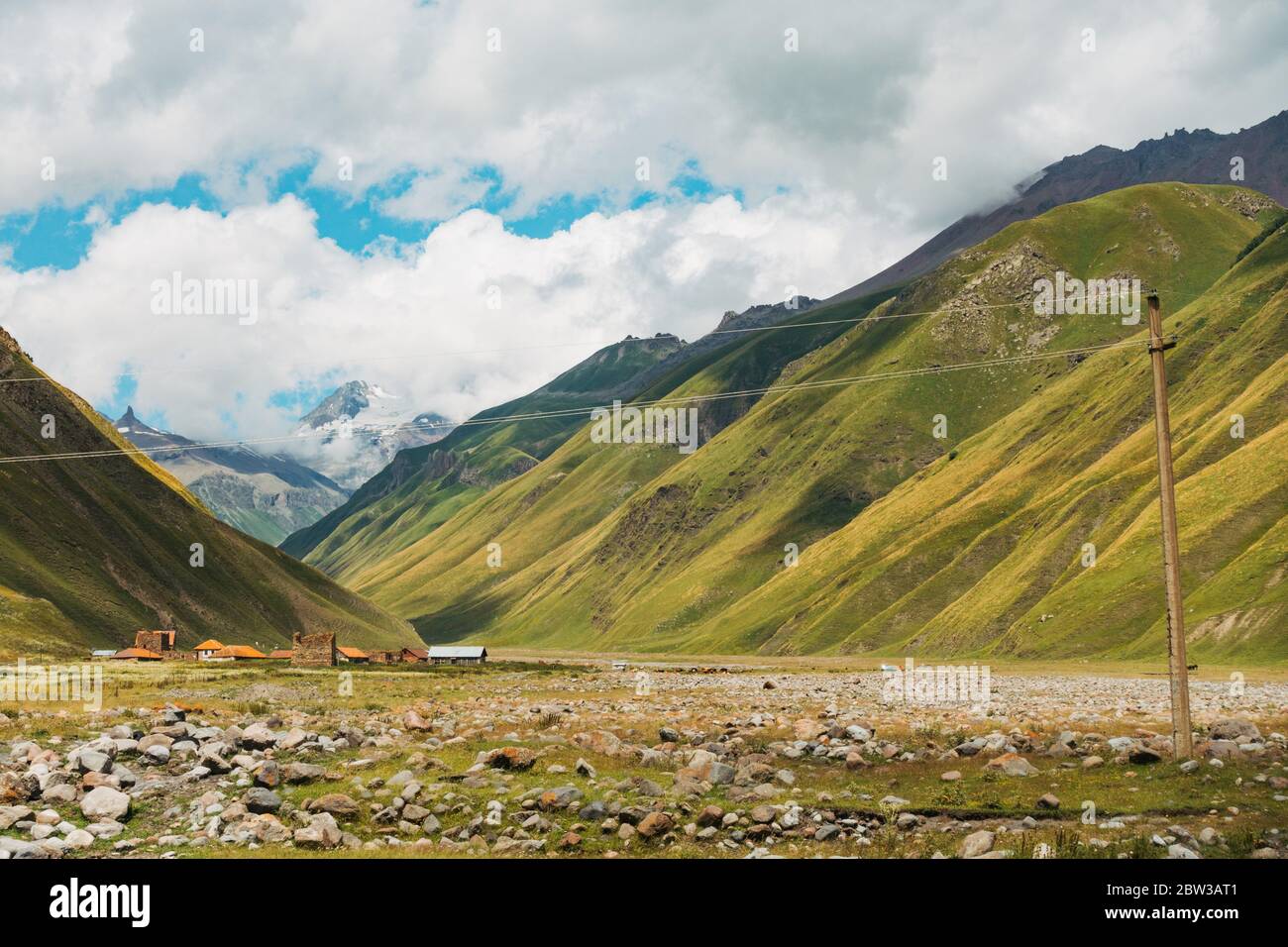 Blick auf das Mnaisistskali Flusstal in der Region Kazbegi, Georgien, während der Sommerzeit. Eine Stromleitung erstreckt sich über den Rahmen Stockfoto