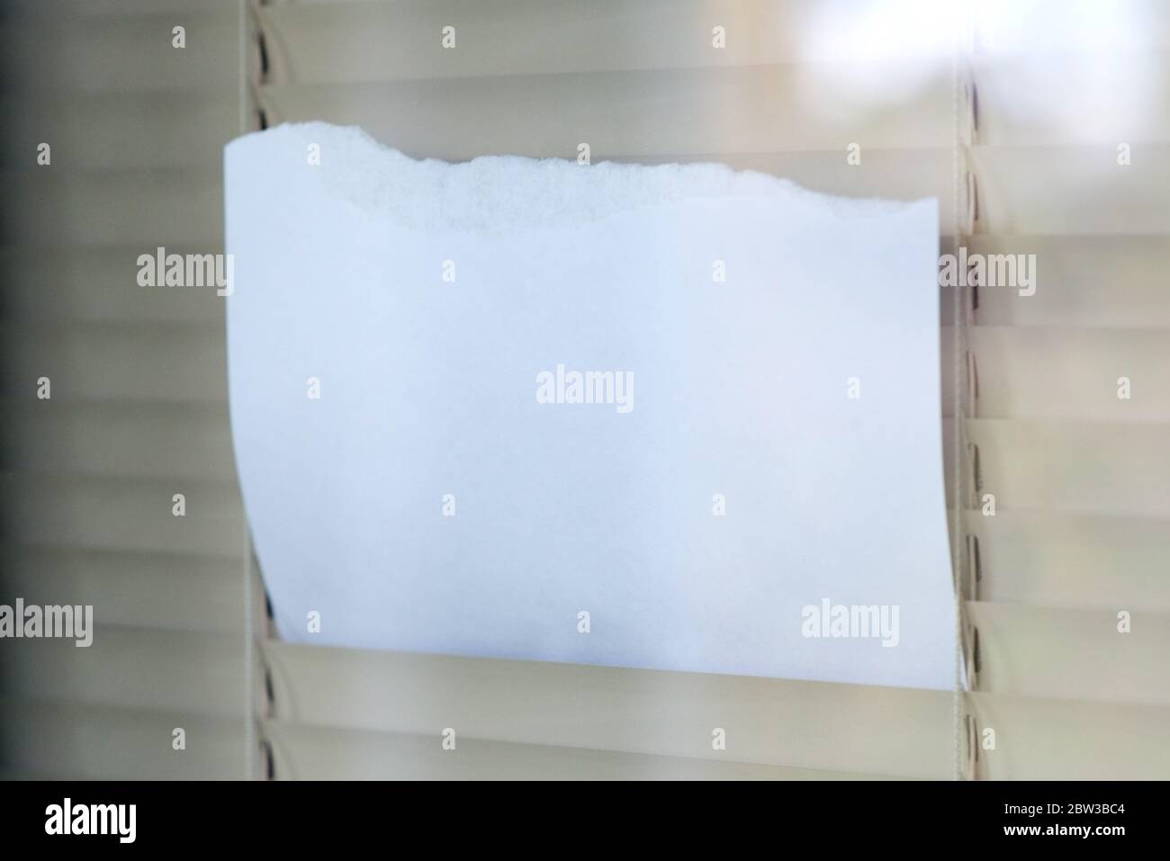 Ein leeres Blatt Papier wird durch das Fenster geschoben Jalousien Stockfoto