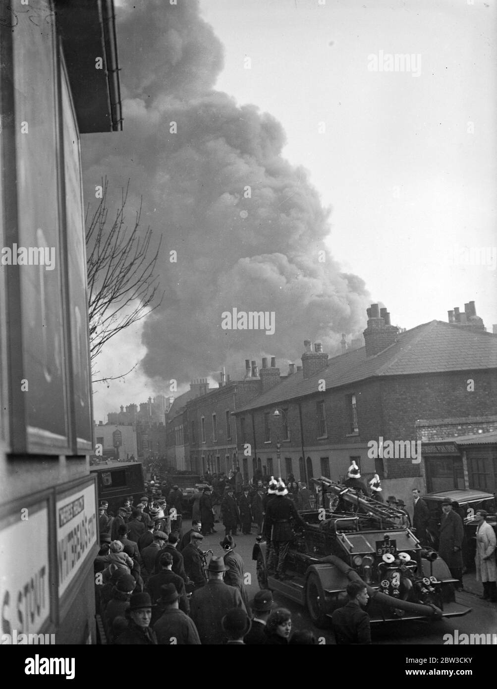 Eine riesige Rauchfasse hängt über den Häusern in Hammersmith, West London, als ein Feuerwehrmann die Straße hinauf geht, um mit dem Brand in einer Reifenfabrik umzugehen. 26. November 1934 Stockfoto