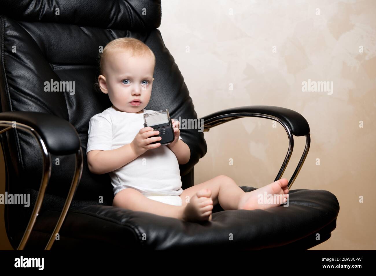 Das kleine Kind sitzt in einem Bürostuhl mit einem Stempel in den Händen Stockfoto