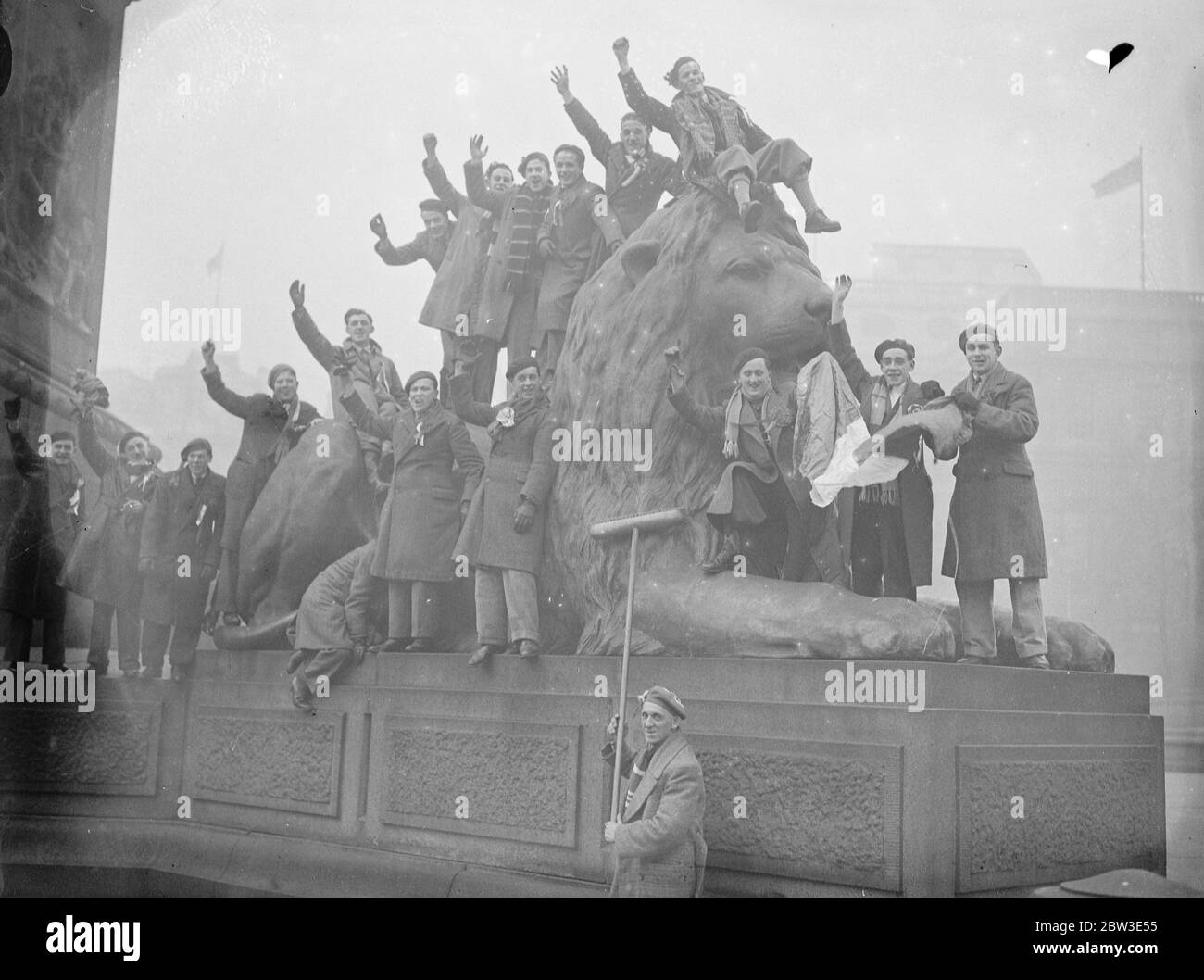 Iren dringen in London ein - der Löwe saß auf. Irische Besucher sitzen auf einem der Löwen am Trafalgar Square. Rugby Internationales Spiel zwischen England und Irland . Februar 1935 Stockfoto