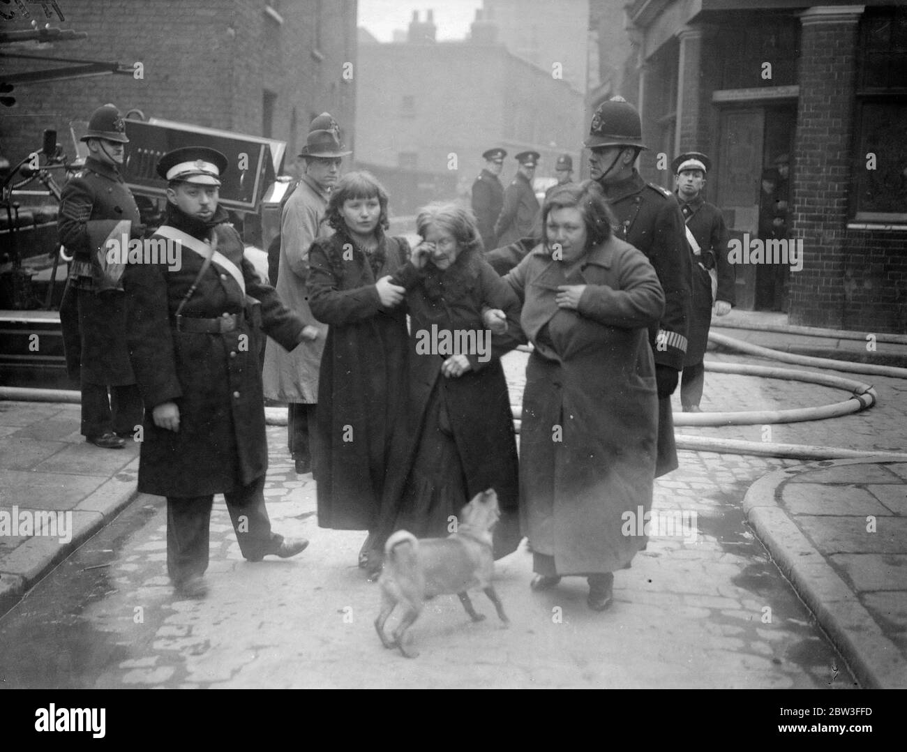 Polizei und die St. John Ambulance Brigade begleiten notleidende Hausbesitzer und ihr Haustier während der Wapping Gas Works lodern aus der Gefahrenzone. 26. Januar 1935 Stockfoto