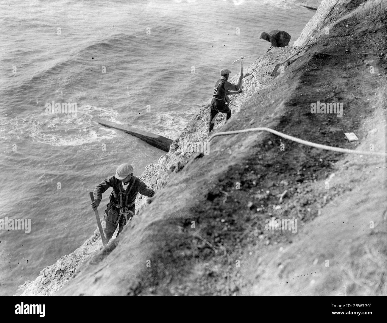 Klippenscheren an Seilen befestigt bei der Arbeit hoch über den Wellen in Rottingdean Clearing gefährliche überhängende Felsen über dem Strandweg . Februar 1935 Stockfoto