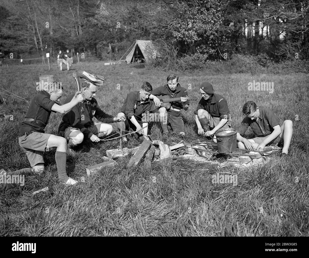 Beste Aufgabe des Tages . Orden der Holzhandwerk Ritterschaft Mitglieder in Sussex, Osterlager. Tragen die malerischen und malerischen Kostüme ihrer Organisation, Mitglieder des Ordens der Holzhandwerk-Chivalry, der Outdoor-Verein für Jugendliche und Mädchen gebildet, haben in Camp in der Nähe von Brighton für Osterferien gegangen. Mitglieder des Ordens sind alle Altersgruppen und kommen aus allen Grafschaften Englands ins Sussex-Lager. Foto zeigt, Einstellung der Kochhäuser Müdigkeit zu Musik im Sussex Camp. 11. April 1936 Stockfoto