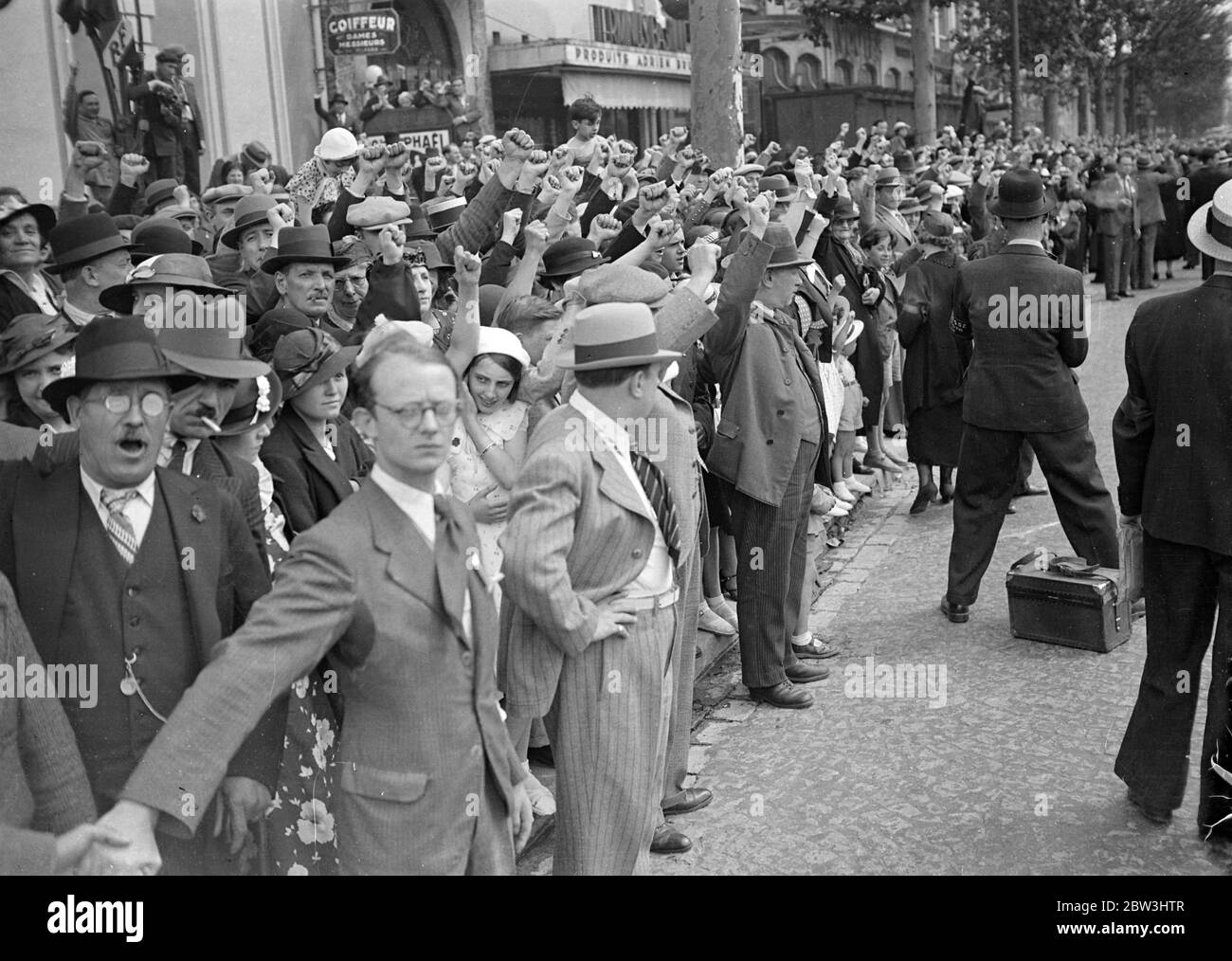 Volksfront Mitglieder Parade In Paris Während Jahrestag Feiern Des Falls Der Bastille . Tausende von Mitgliedern der Volksfront, angeführt von ihren Führern, marschierten durch die fröhlich geschmückten Straßen von Paris in Monster Prozessionen während der Jubiläumsfeiern des Falls der Bastille in der Französischen Revolution. Große Kräfte der Polizei und mobile Wachen patrouillierten auf den Straßen, um Unruhen zu verhindern. Foto zeigt: Die Zuschauer grüßen die Kommunisten, während die Prozessionen durch die Straßen von Paris gehen. Juli 1936, 14 Stockfoto