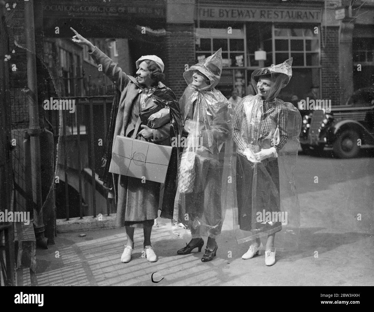 Invisible Protection Against English Summer - American Girls stellen neue Mode in London VOR EINE Party amerikanischer Mädchen aus Chicago hat London eine neue unsichtbare Mode während einer Europatour vorgestellt. Es ist wasserdicht Umhang komplett transparent und wiegt nur zwei Unzen. Das Cape ist 10 Prozent. Gummi und wenn nicht in Gebrauch Falten in einem Umschlag sechs Zoll durch vier. Es kostet etwa vier Schilling und bietet Abdeckung von Kopf bis Fuß. Foto zeigt: Die Mädchen tragen ihre transparenten Umhänge, als sie DR inspiziert. Johnson ' s Haus in der Stadt . Juli 1936, 13 Stockfoto