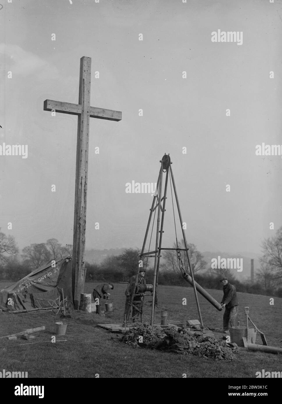 Die Vorarbeiten an der neuen Kathedrale von Guilford beginnen im Schatten des Kreuzes. Mit dem Untergang einer Bohrmaschine im Schatten eines riesigen Holzkreuzes in Guilford haben die Vorarbeiten an der neuen Kathedrale begonnen, die in der Stadt Surrey County gebaut werden soll. Arbeiter sinken die Bohrmaschine, um die Art des Bodens zu bestimmen, in dem die Grundlagen des Bodens gelegt werden. Der Bohrer, der hohl ist, ermöglicht Proben der Erde, durch die es geht, für die Bauherren Inspektion gebracht werden. Foto zeigt , Sinken der Bohrer im Schatten des Holzkreuzes Kennzeichnung der Website Stockfoto