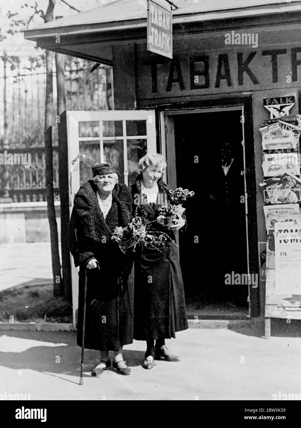 Baroness Opernsängerin besitzt jetzt Kiosk. Annie Dirkens (Baroness Hauenstein), einst eine der berühmtesten Opernsängerinnen Wiens, ist heute Inhaberin eines Zeitungskiosk in der Nähe der Burgthester in Wien. Foto zeigt, Baroness Annie Dirkens Hauenstein (links) mit ihrer Tochter vor dem Kiosk. 20. April 1936 Stockfoto